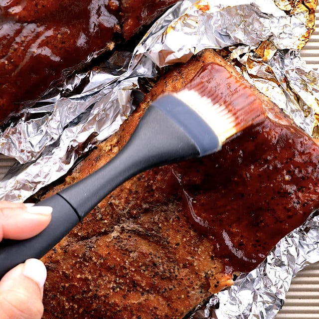BBQ sauce being brushed generously on tender oven-baked ribs.