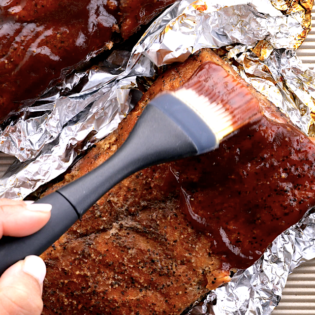 BBQ sauce being brushed generously on tender oven-baked ribs.