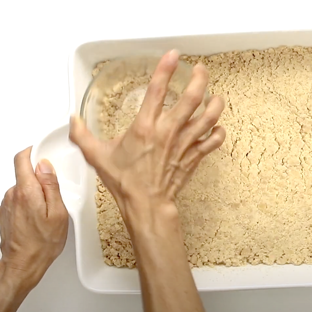 Crust mixture being pressed into a greased pan to make blueberry crumb bars.