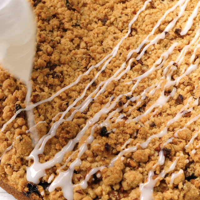 Icing being drizzled over freshly baked blueberry coffee cake.