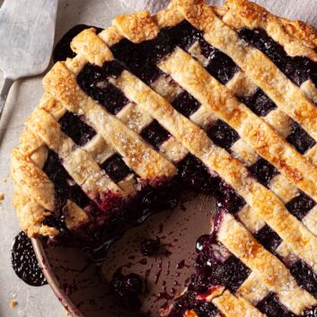 overhead image of a blueberry pie with a lattice crust topping and a slice cut out
