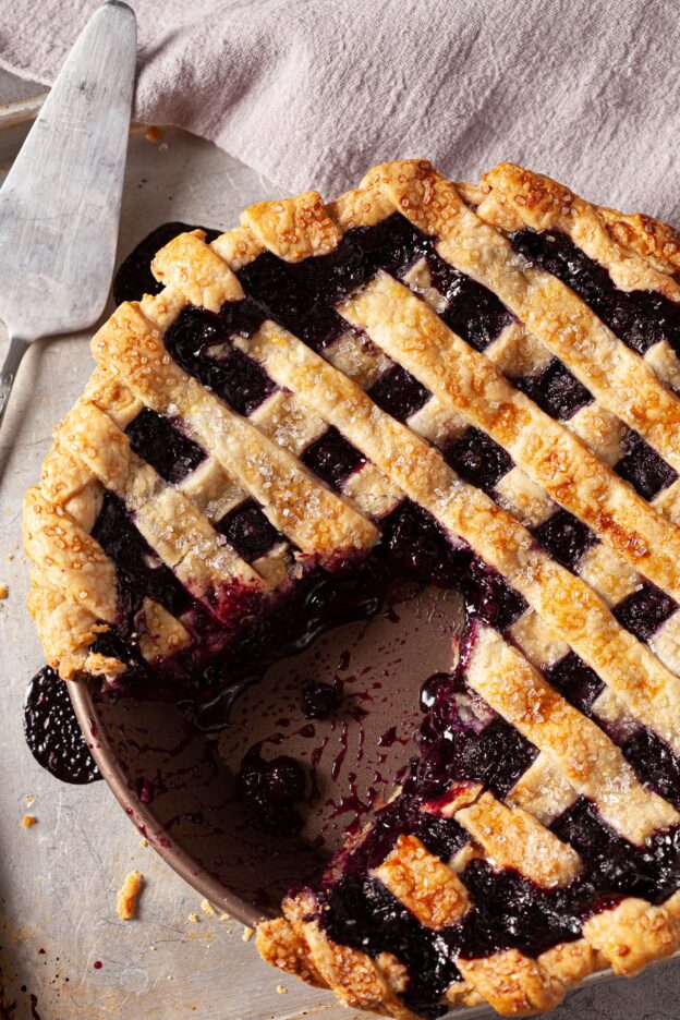 overhead image of a blueberry pie with a lattice crust topping and a slice cut out