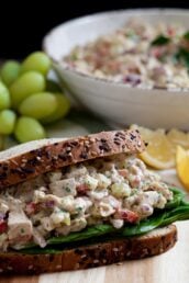 a healthy chicken salad sandwich with green grapes and a bowl of chicken salad in the background