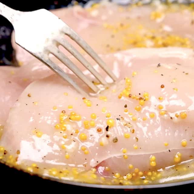Chicken being pierced with a fork with a lemon marinade on top.