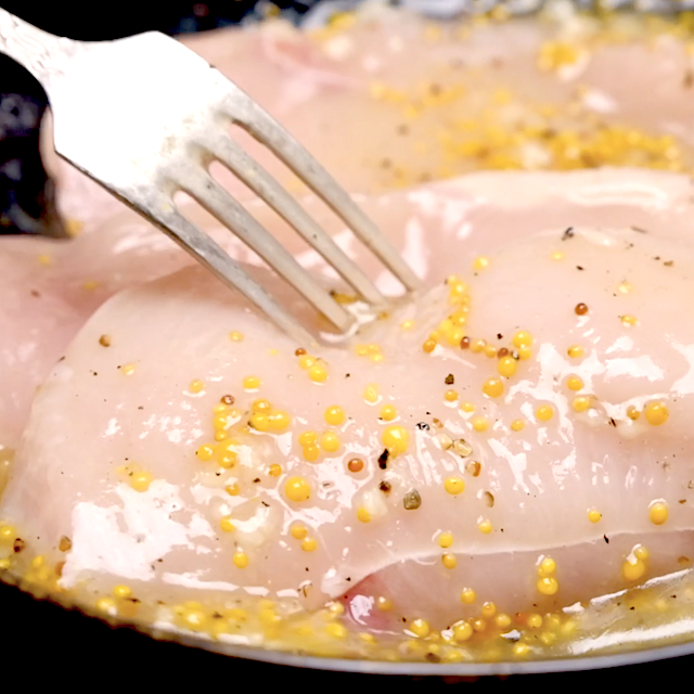 Chicken being pierced with a fork with a lemon marinade on top.