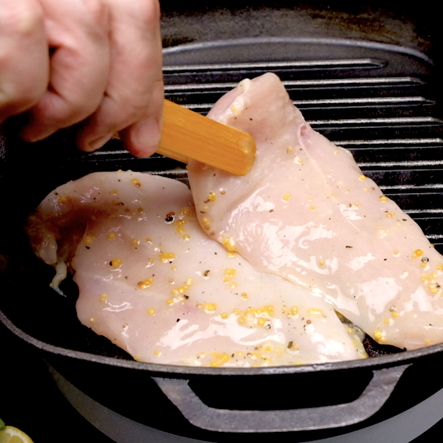 Marinated lemon chicken being placed on a grill to make grilled lemon chicken.