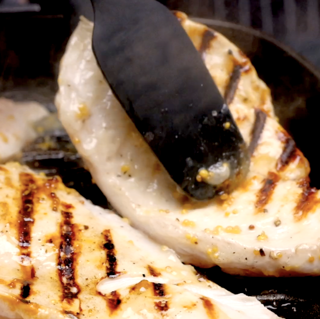 Grilled lemon chicken being flipped in a grill with visible grill marks on top.
