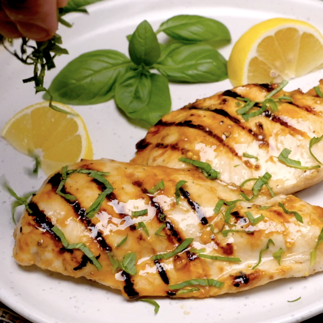 Fresh herbs being sprinkled on top of grilled lemon chicken before serving.
