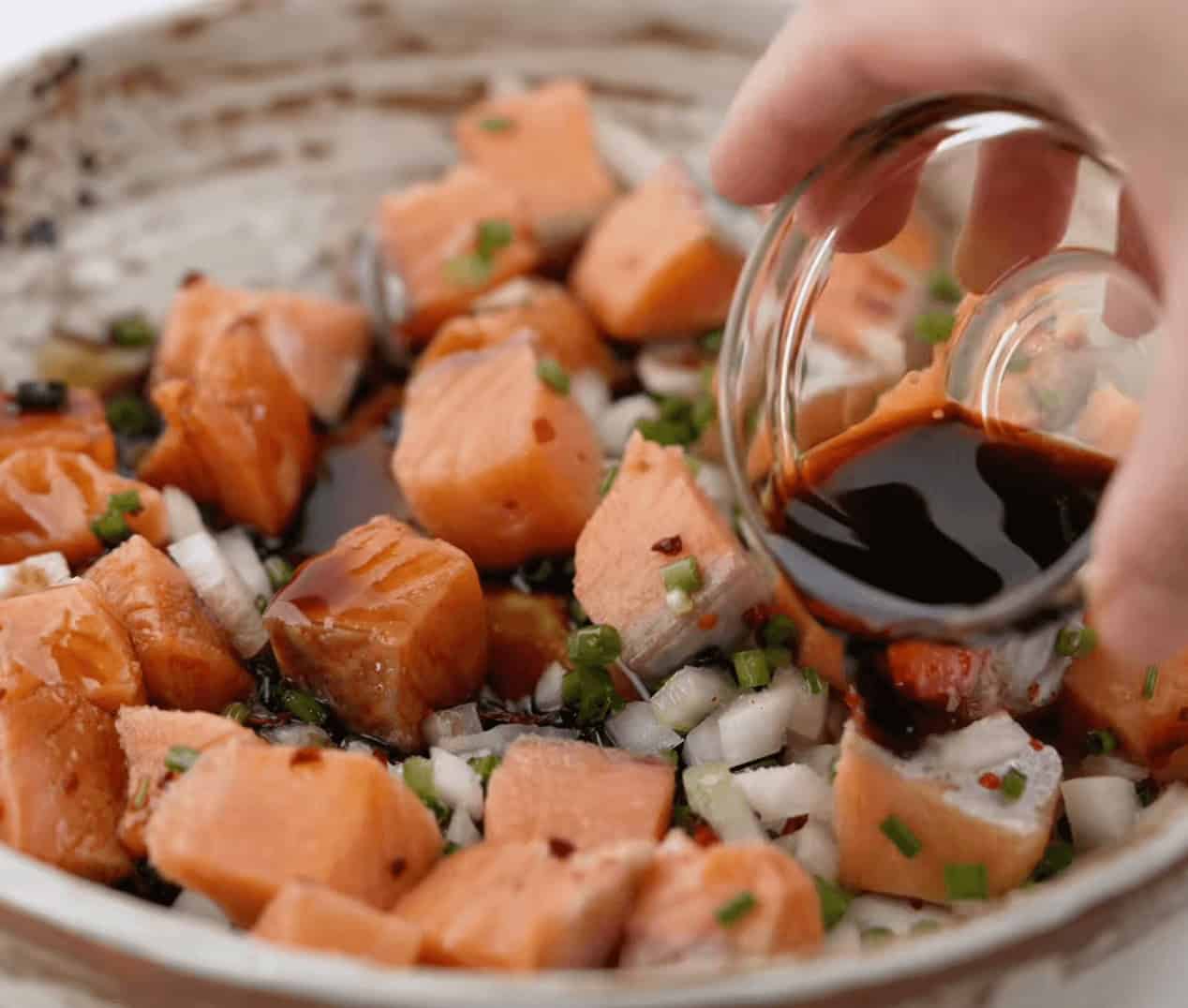 Pouring the sauce and seasonings over the top of the salmon poke bowl ingredients.