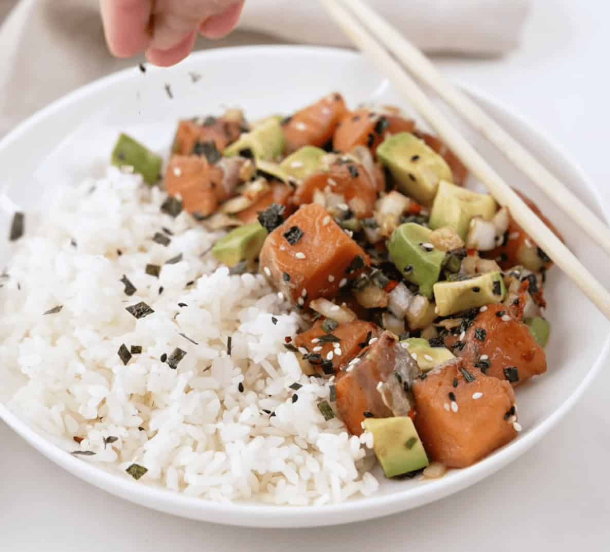Topping the salmon poke bowl and rice with garnish.
