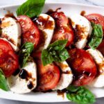 caprese salad topped with balsamic on a white plate