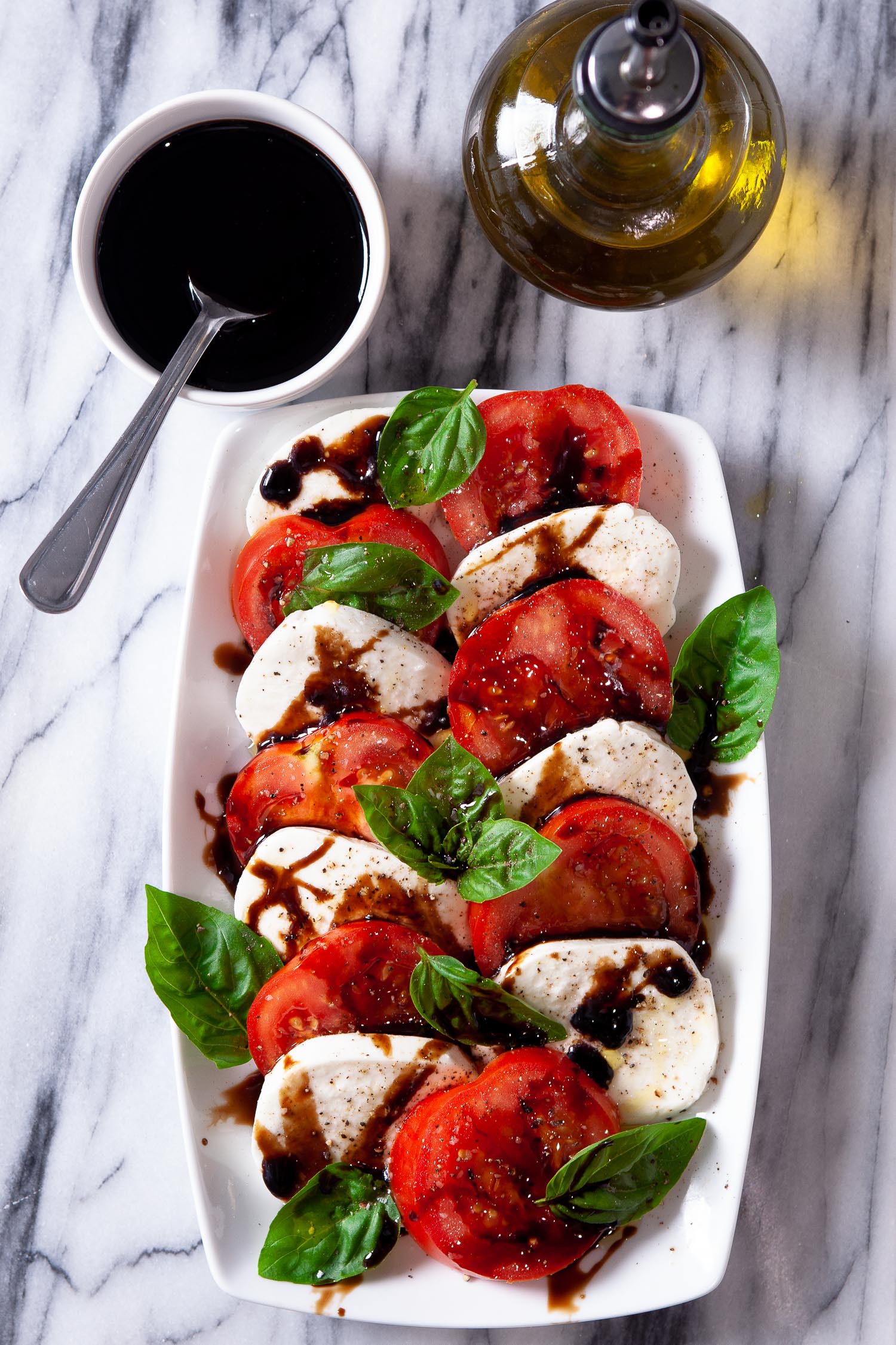 Caprese salad on a white rectangular plate with balsamic and olive oil on the side