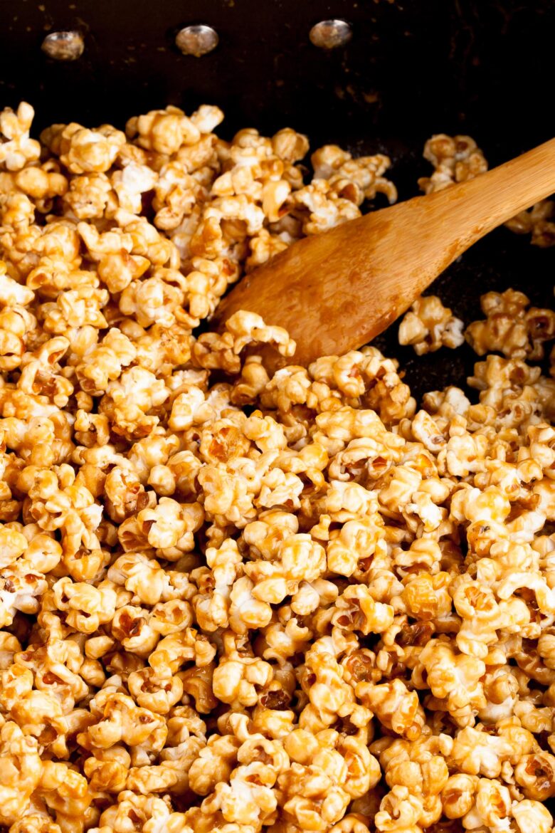 caramel popcorn being stirred with a wooden spoon