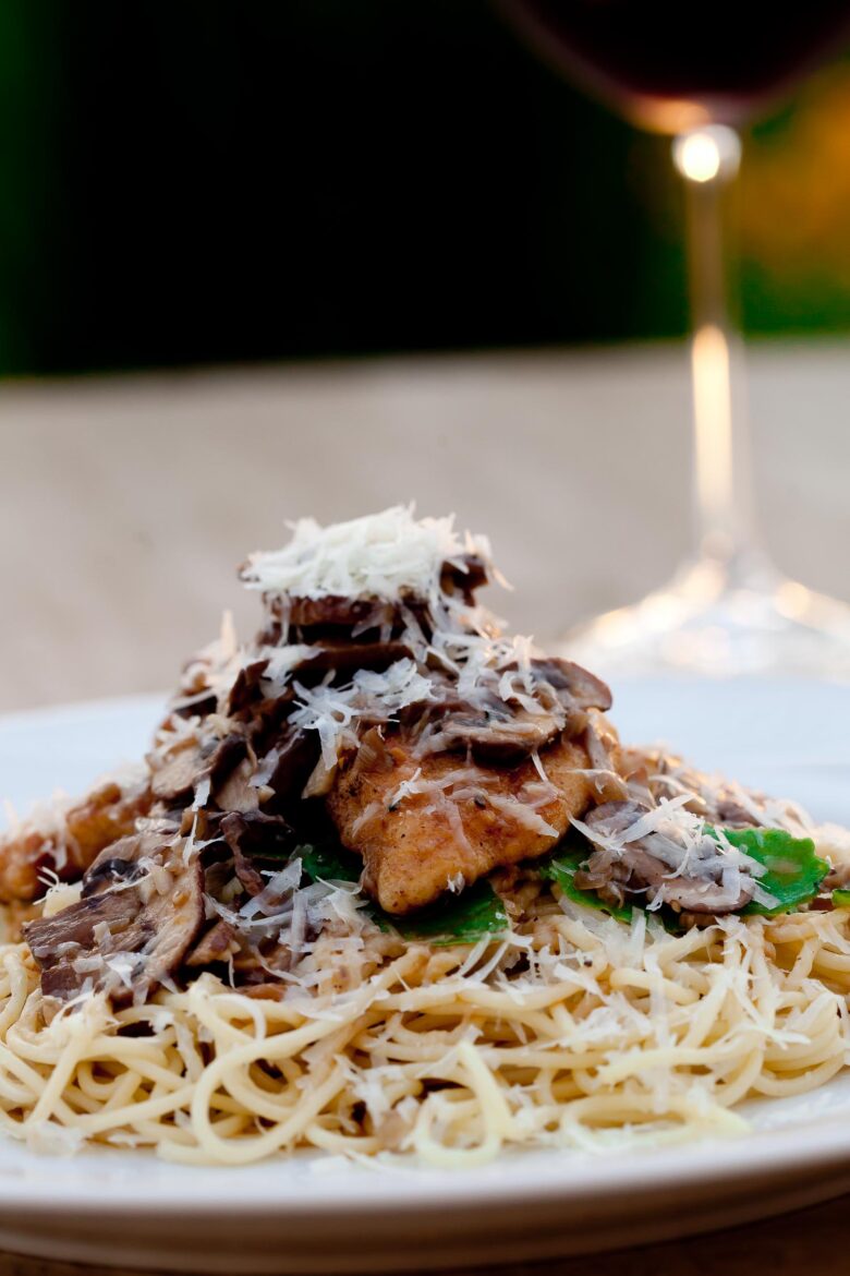 a bowl of cooked chicken marsala with mushrooms on top of angel hair pasta