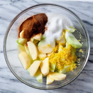 overhead image of a glass bowl full of sliced apples, cinnamon, sugar, and lemon zest for a gluten free apple crisp filling