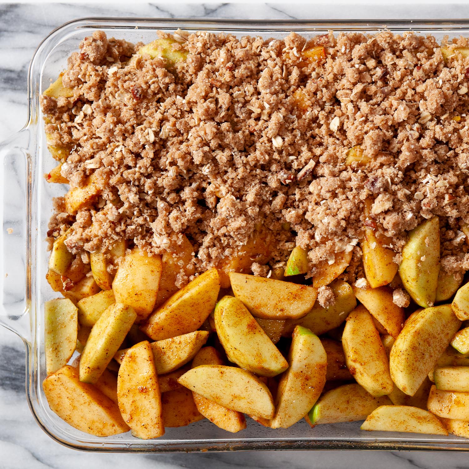 overhead image of spiced apples in a glass baking dish with one side topped with an oat topping