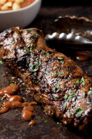 a grilled pork tenderloin with tongs next to it