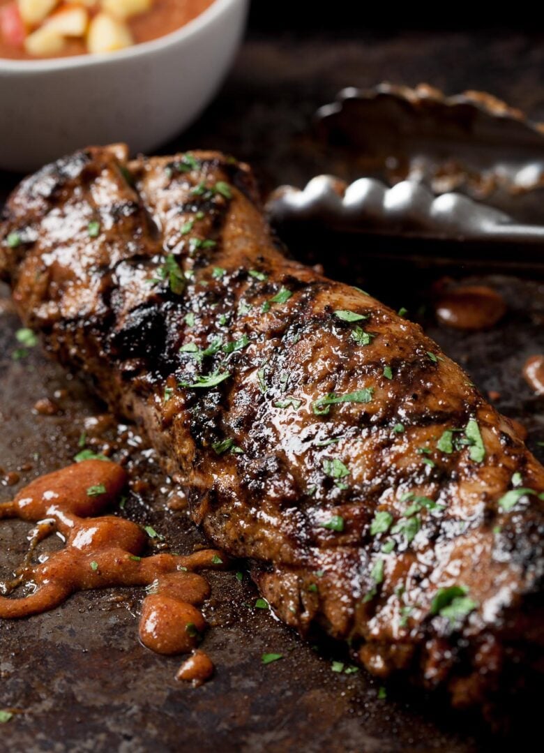 a grilled pork tenderloin with tongs next to it