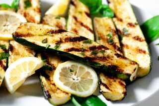 grilled zucchini on a plate with lemon wedges