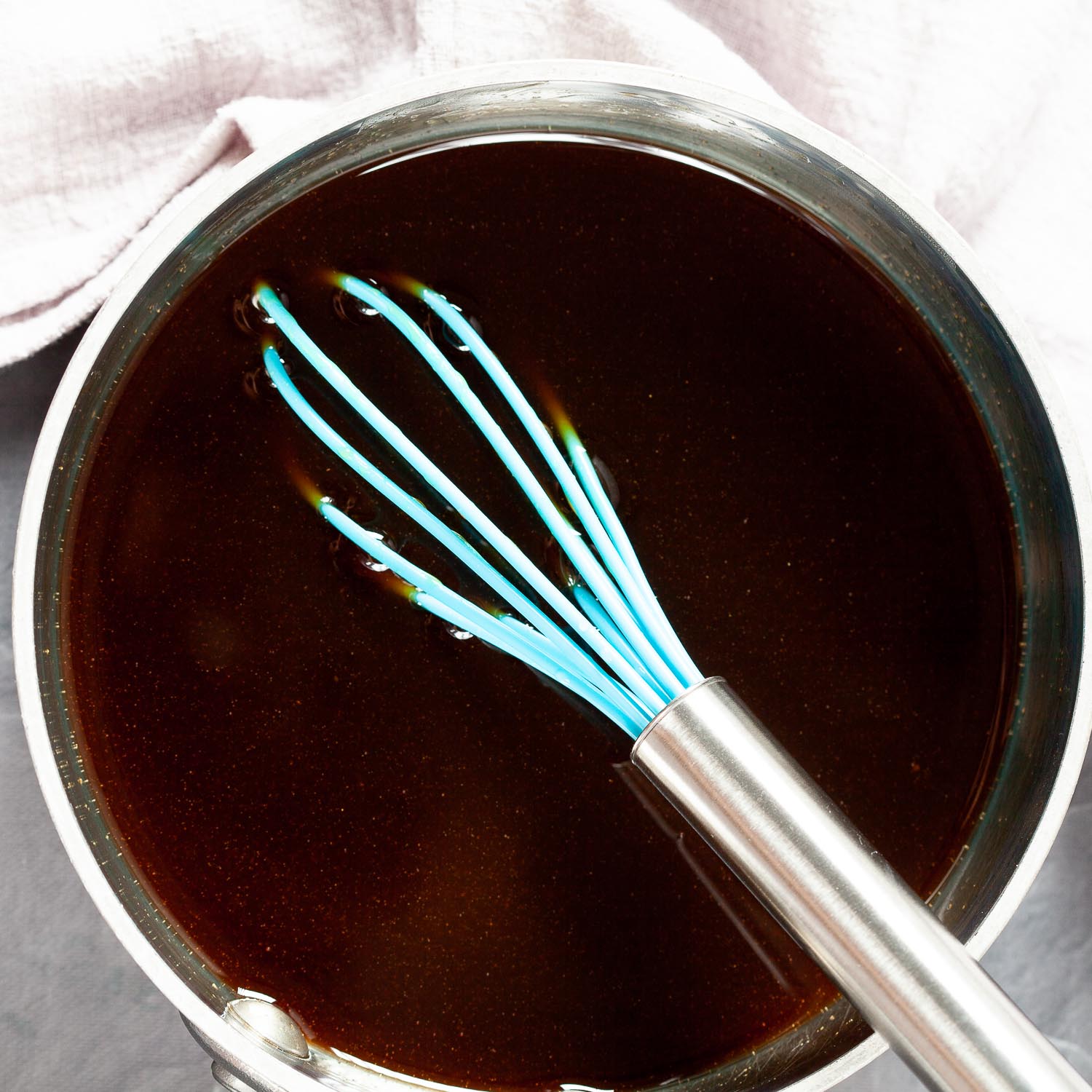 overhead image of a saucepan full of teriyaki sauce with a blue whisk sticking out