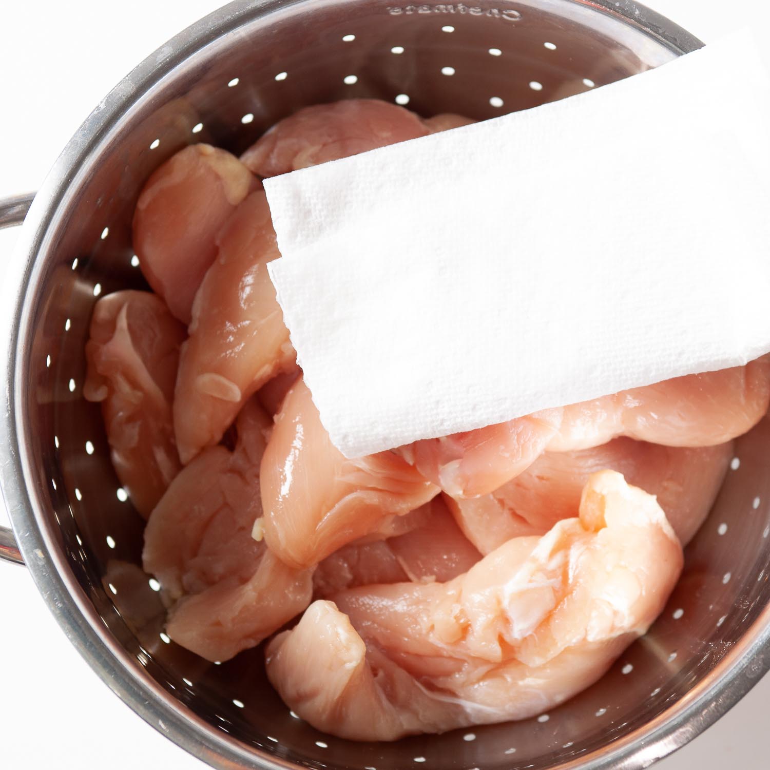 chicken in a colander being pat dry with a paper towel