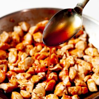 a spoon drizzling teriyaki sauce on top of chicken pieces in a skillet