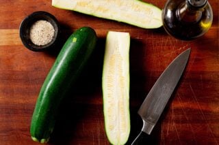 whole zucchini being sliced on cutting board
