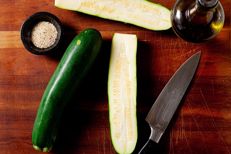 whole zucchini being sliced on cutting board.