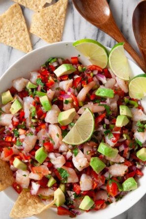 shrimp ceviche in a white bowl with tortilla chips and lime wedges