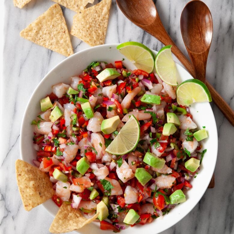 shrimp ceviche in a white bowl with tortilla chips and lime wedges