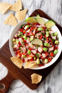 overhead image of a white bowl full of shrimp ceviche topped with lime wedges and tortilla chips