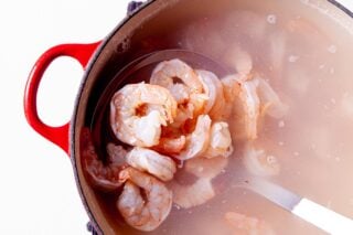 a ladle scooping boiled shrimp out of a pot