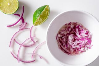 overhead image of a bowl full of chopped red onion with red onion strips and lime wedges on the side