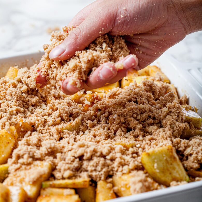 assembling the best apple crisp in a baking dish with apple filling and cinnamon oat topping