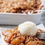 Apple Crisp being served on a white plate with a scoop of vanilla ice cream on top.