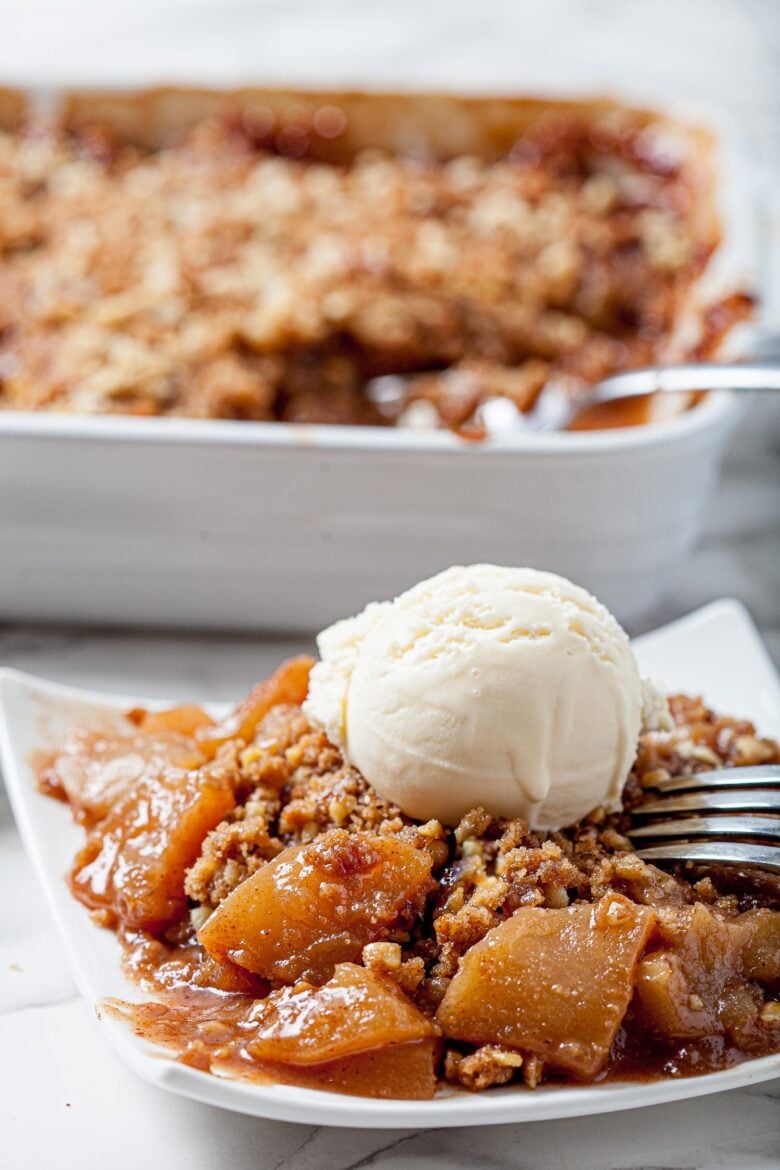 homemade apple crisp on a white plate with a scoop of vanilla ice cream and a fork