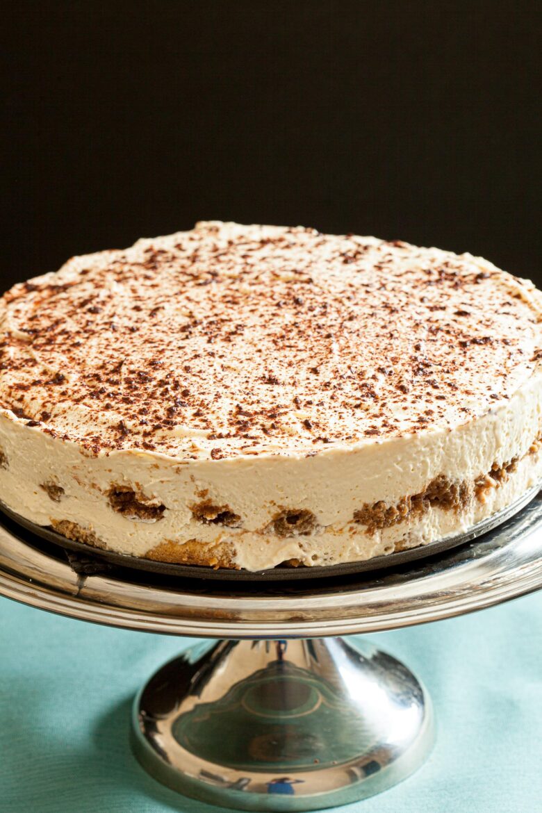 a tiramisu cake on a cake stand without ladyfingers around the edges