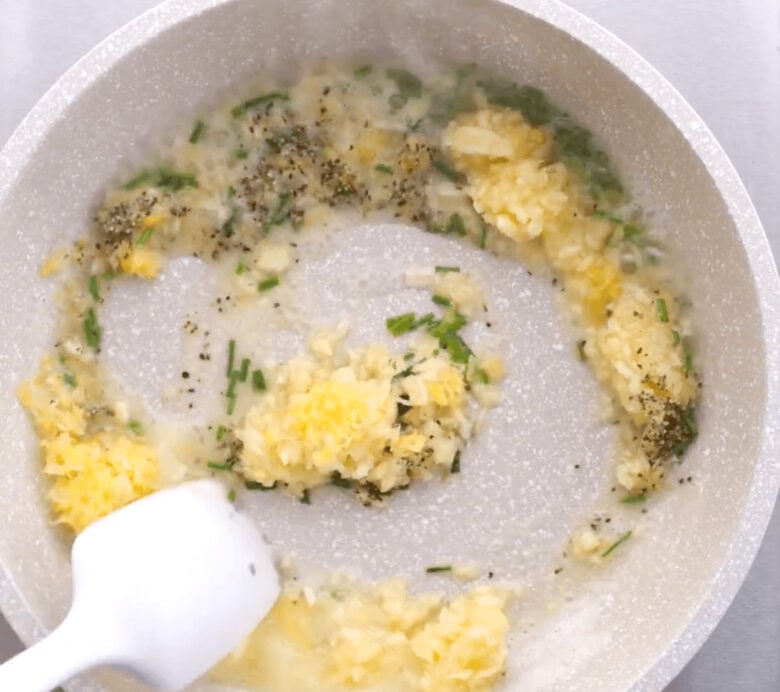 Ingredients to make the lemon garlic butter sauce in a pan being stirred by a white rubber spatula.