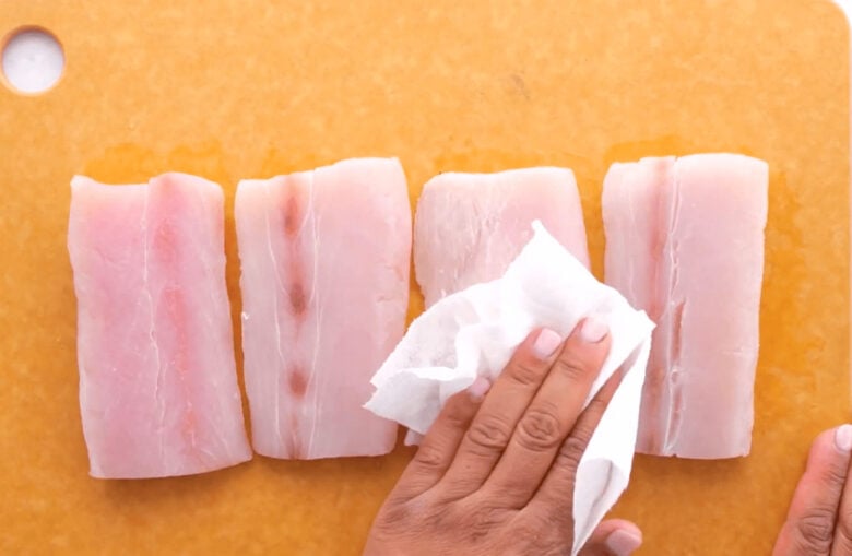 Hand holding a clean paper towel patting the mahi mahi fillets dry.