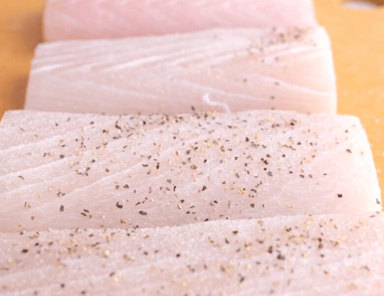 Salt and pepper being added to both sides of the mahi mahi fillets.
