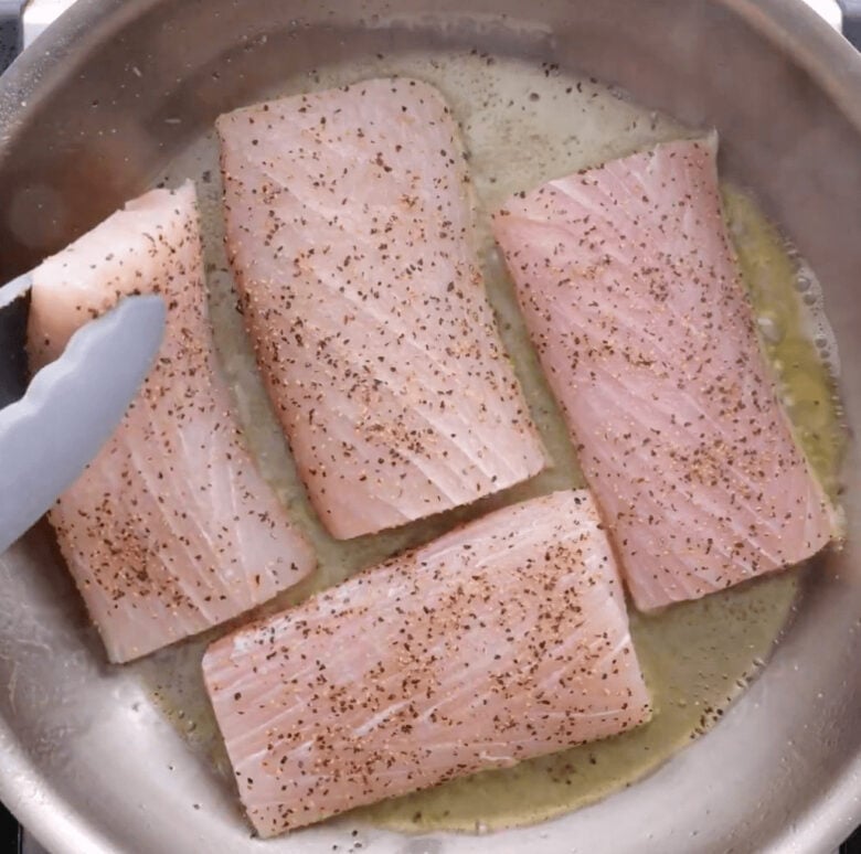 Adding the mahi mahi fillets to the hot skillet to cook.