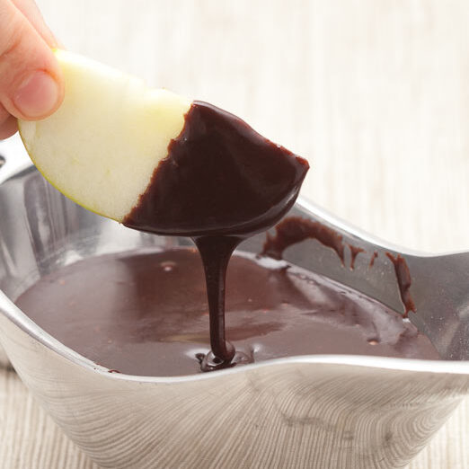 an apple slice being dipped into hot fudge sauce
