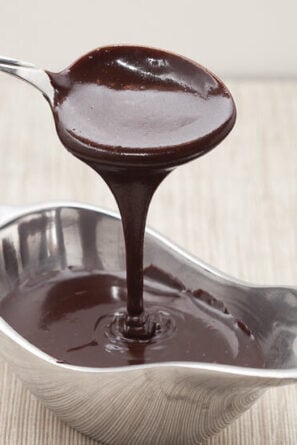 a bowl of hot fudge sauce with a spoon drizzling the fudge sauce above it