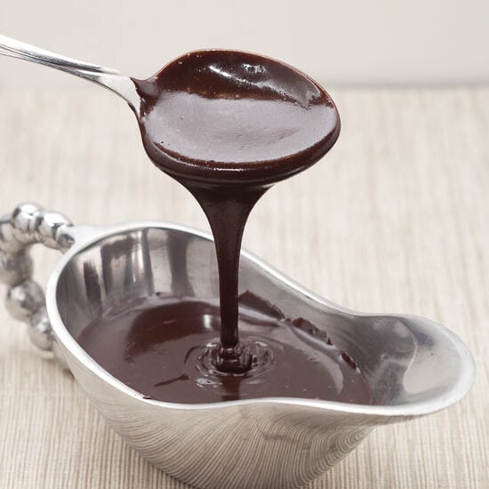 a bowl of hot fudge sauce with a spoon drizzling the fudge sauce above it