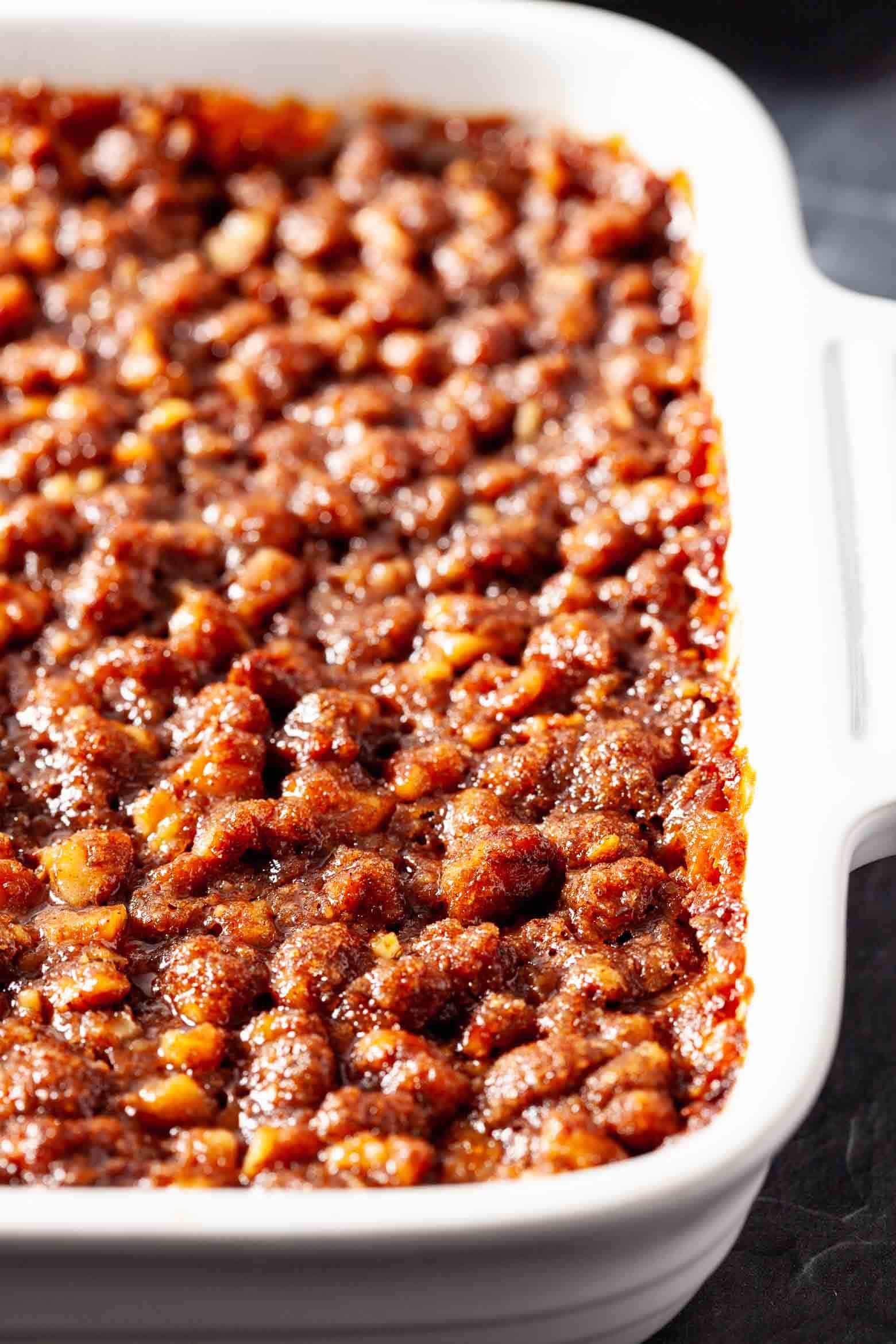Sweet potato casserole with pecan crumble topping in a white baking dish.