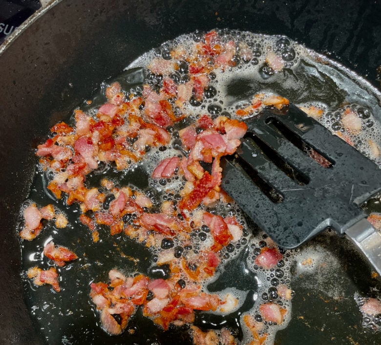 bacon being cooked in a skillet. 