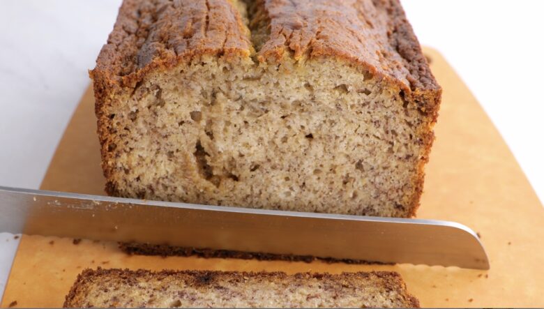 Loaf of banana bread being sliced on cutting board