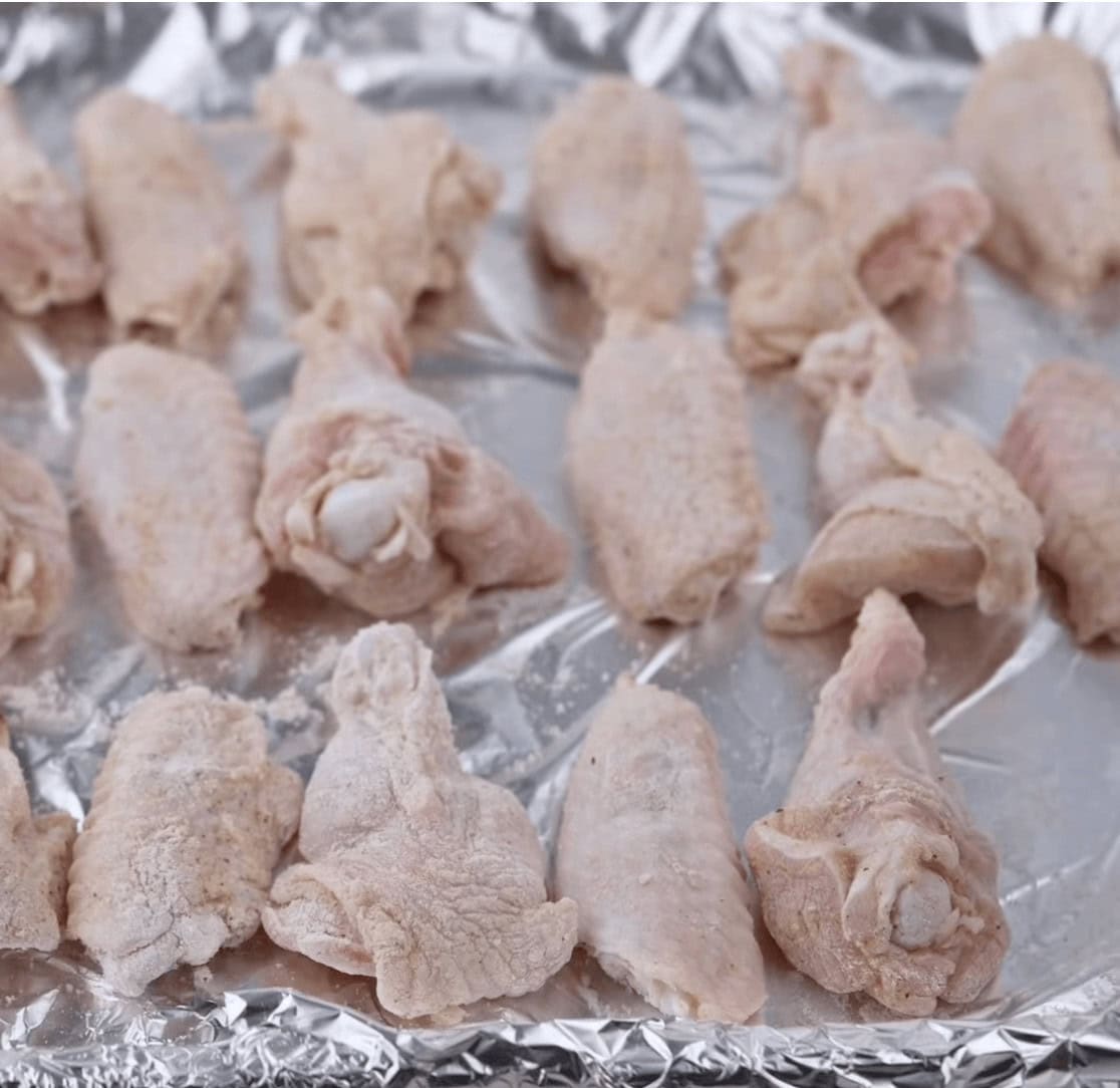Chicken wings arranged on a foil-lined baking sheet, coated with cornstarch.