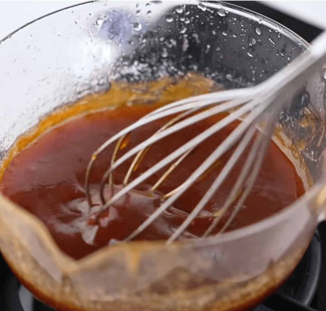 Using a whisk to combine all the sauce ingredients in a clear bowl.
