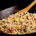 Fried rice with ham and veggies in a wok with a brown serving spoon.